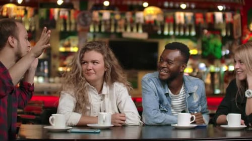 Student Meeting in a Restaurant and Cafe. A Man in a Shirt Tells a Story To Friends, Two Girls and