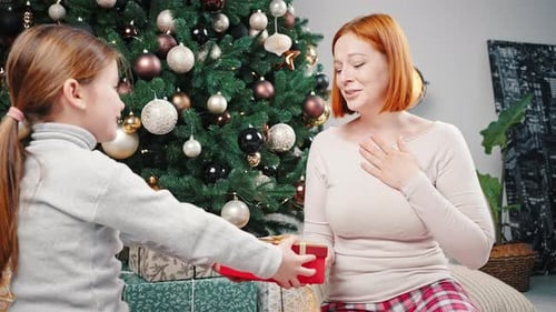 Girl Giving Red Christmas Gift to Smiling Woman
