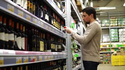 Young Man with Black Hair and Beard Chooses Red Wine Gift