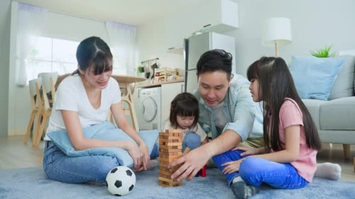 Attractive parent mother and father play tumbling tower wood block game with young daughter at home.