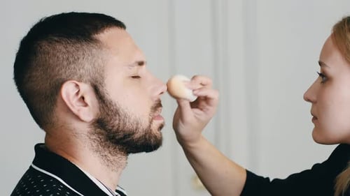 Woman Applying Makeup to Man's Face with Sponge