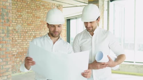 Dois homens de capacete olham para o plano do edifício