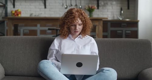 Woman works on laptop at home on sofa