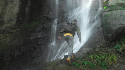 man with backpack on his back is walking alone to waterfall in depths jungle.