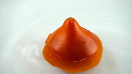 Rotating ripe tomato in water on a white background. Slow motion.