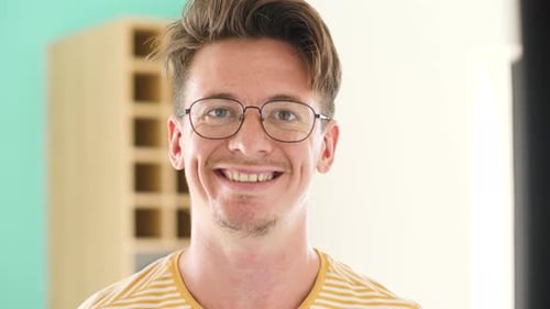 Porträt eines jungen klugen Mannes mit Brille, der in die Kamera lächelt.
