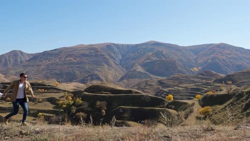 Couple Runs Along Hill with Dry Grass Against Cascade Slope