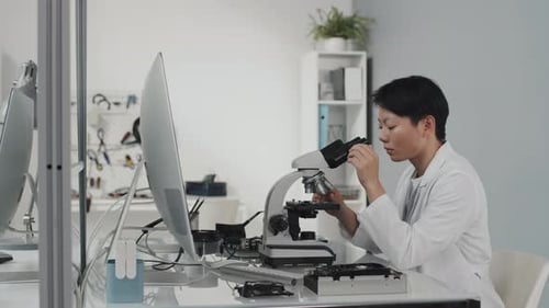 Asiatische Ingenieurin arbeitet mit Mikroskop und Computer im Labor