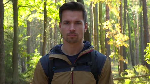 A Young Handsome Hiker Looks Seriously at the Camera in a Forest