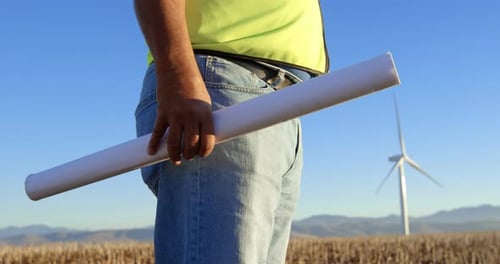 Male engineer standing with blueprint in the wind farm