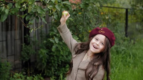 Young Girl Plucked Ripe Apple From Tree in Fruit Garden. Smiling Teen Girl in Beret and Coat Holding