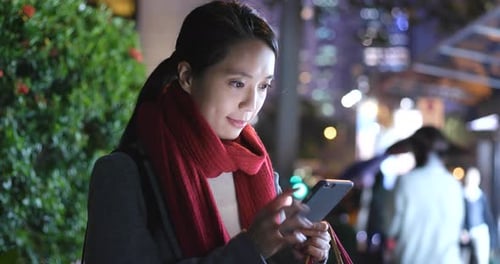 Woman use of mobile phone and hold shopping bag in city at night