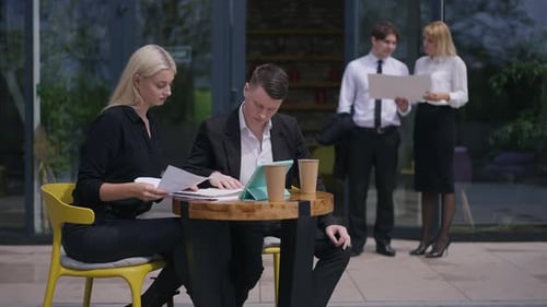 Concentrated Young Coworkers Sitting on Terrace Analyzing Project As Blurred Colleagues Standing at