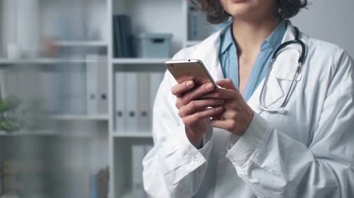 Una doctora con un teléfono móvil en bata de laboratorio está hablando por teléfono. El médico trabaja y busca