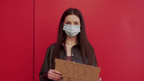 Woman Wearing Mask Holds Sign Saying "STOP COVID-19"