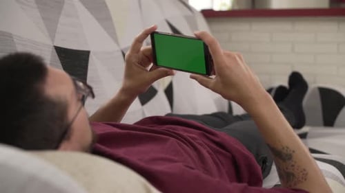young man lying on the couch staring at his cell phone, green screen