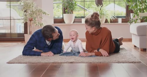 Smiling Young Couple Lying Together on Rug on Their Living Room Floor at Home with Their Adorable