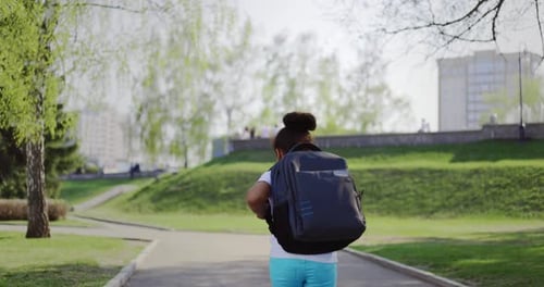 Schulmädchen mit Rucksack rennt an einem sonnigen Tag aus ihrem Schultraum im Park nach Hause