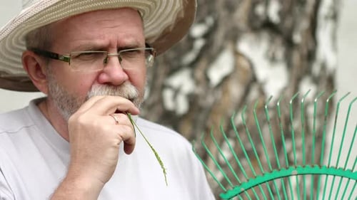 Man with Grass in Mouth Holding Rake