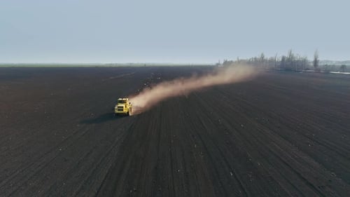 Tractor in the Large Brown Field Prepares the Soil for Sowing