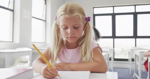 Video of happy caucasian girl sitting at school desk and learning