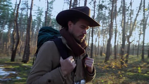 Backpacker with Camera Walks Along a Trail in the Forest