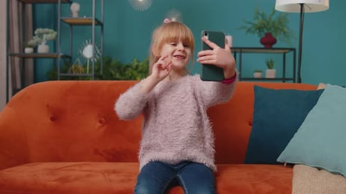 Little Toddler School Kid Girl Taking Selfie Photo with Smartphone While Sitting on Sofa at Home