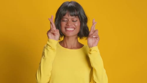 Woman Crossing Fingers for Luck on Yellow Background