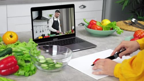 Mujer en la cocina Estudia en línea, videollamada, cámara web, portátil, rebanadas de tomate, escucha chef