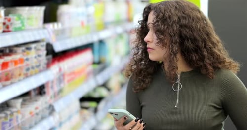 Young Attractive Woman Checking to Do List on Smartphone in Supermarket