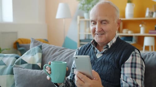 Senior Man Using Smartphone and Drinking Coffee at Home