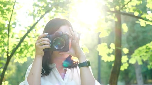 Pretty Smiling and Laughing Girl Photographer Wearing White Shirt Is Making Photos in a Park
