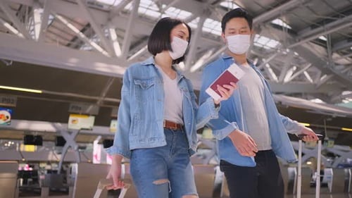 Asian man and woman passenger couple wearing face mask walking in airport terminal to boarding gate.