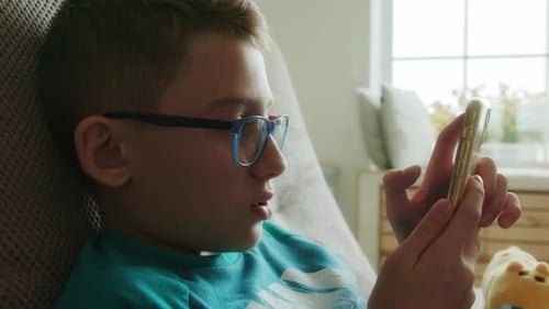 Cute Teenager in a Green Tshirt Uses His Smartphone While Laying on the Couch