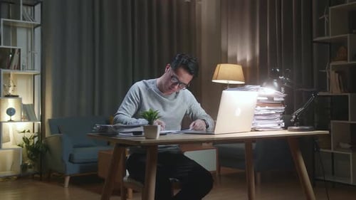 Man Working at Desk with Laptop at Night