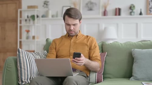 Young Adult Using Laptop and Phone on Couch
