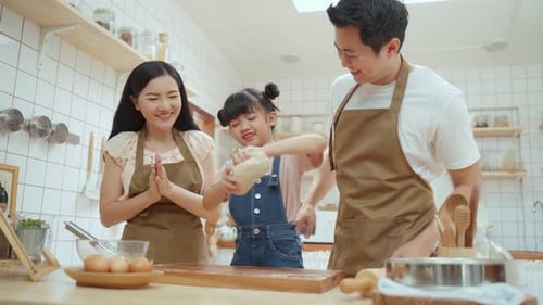 Asian happy family spending time in kitchen together, parent teaching young daughter bake bakery.