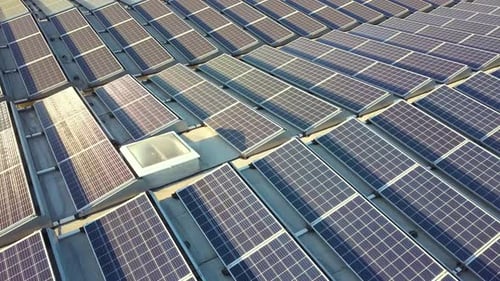 Aerial view of many photo voltaic solar panels mounted of industrial building roof.