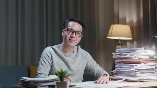 Asian Man Smiling To Camera While Working With Documents At Home