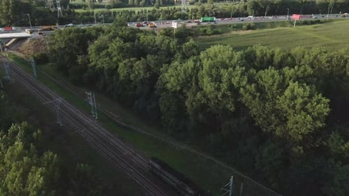 Eine Rangierlokomotive bewegt sich auf Schienen. Auf beiden Seiten der Eisenbahn wachsen Bäume. Luftbildfotografie.