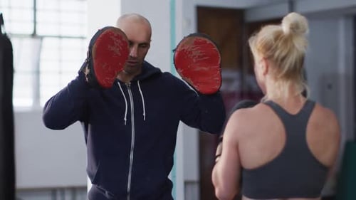 Caucasian female boxer wearing boxing gloves training her punches with male trainer at the gym