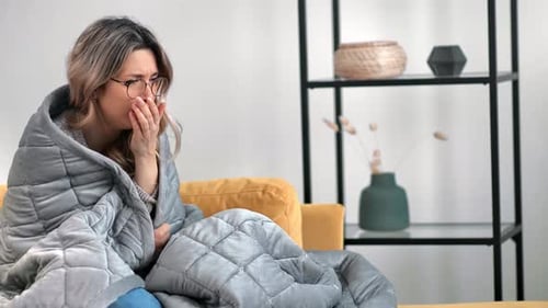 Une femme malade tousse et se refroidit, enveloppée dans une couverture, premiers symptômes de la grippe