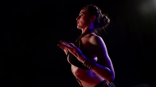 Eine Frau im Profil tanzt im Studio einen orientalischen Tanz auf schwarzem Hintergrund und macht schön