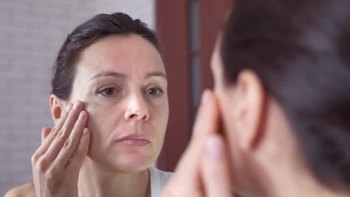 Woman Applies Makeup to Face in Mirror