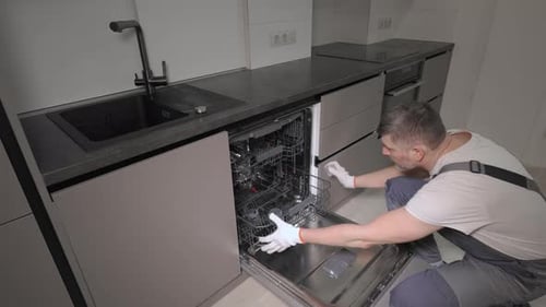 Ein professioneller Mechaniker in Overalls überprüft einen Haushaltsgeschirrspüler in der Küche