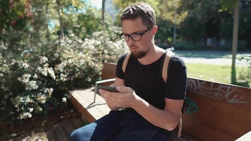 Alone Male Tourist Is Viewing on Screen of His Smartphone, Sits in Park Area