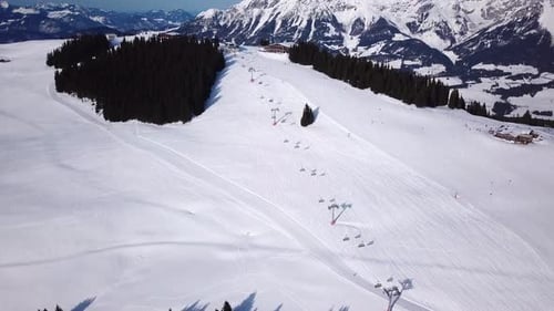 Ski resort in sunny weather. Snow on the ski slope of a wooded mountain. Many tourists near the ski
