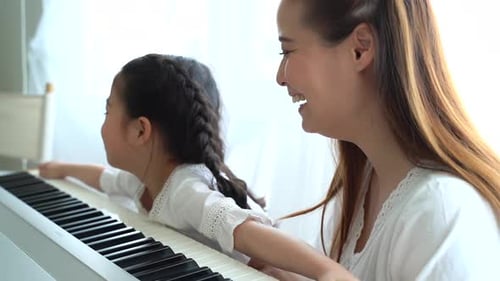 Child Learns Piano with Adult Woman's Help