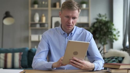 Man Celebrates Success Using Tablet at Desk