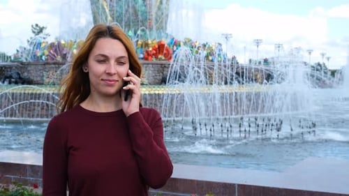 Pretty Woman Talking on Mobile Phone on the Background of the Fountain